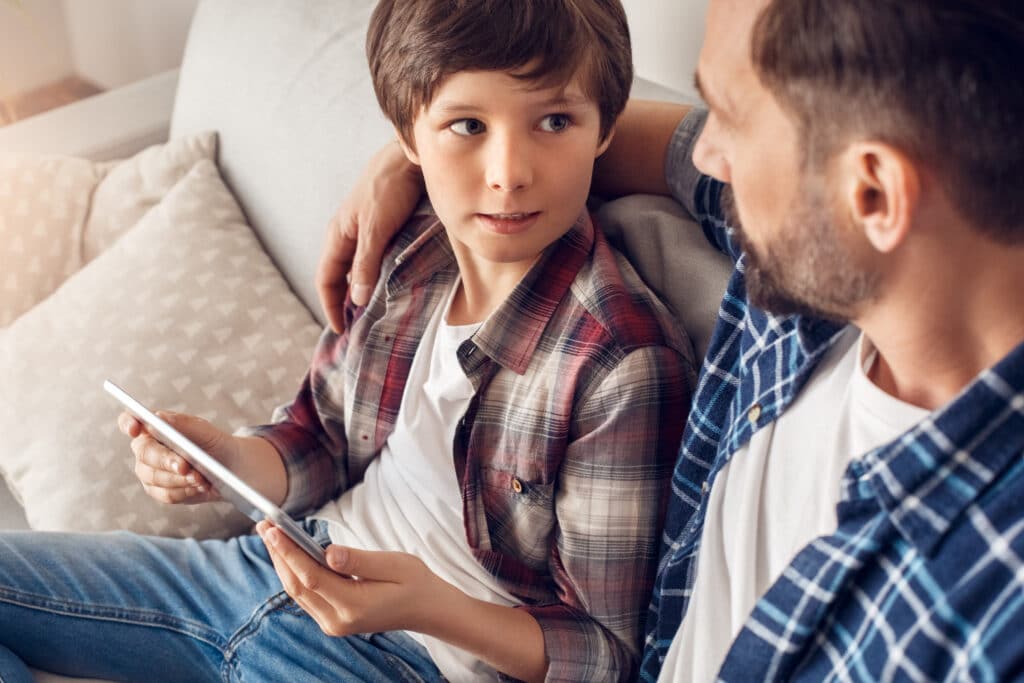 little boy on tablet with dads arm around him