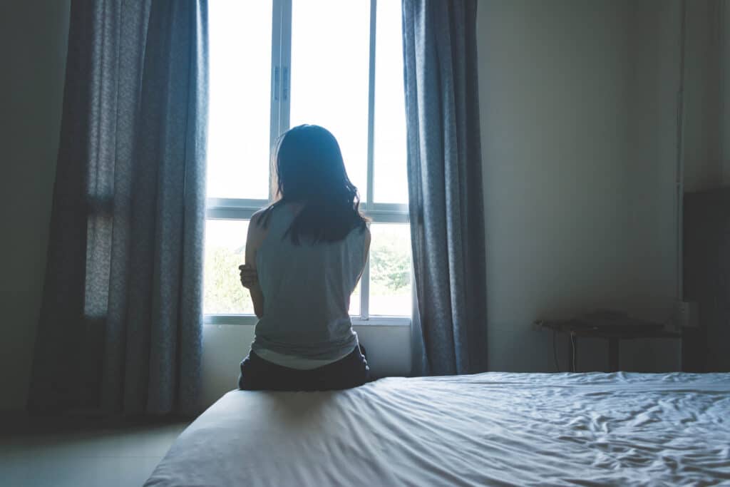 sad teen sitting on bed looking out a window